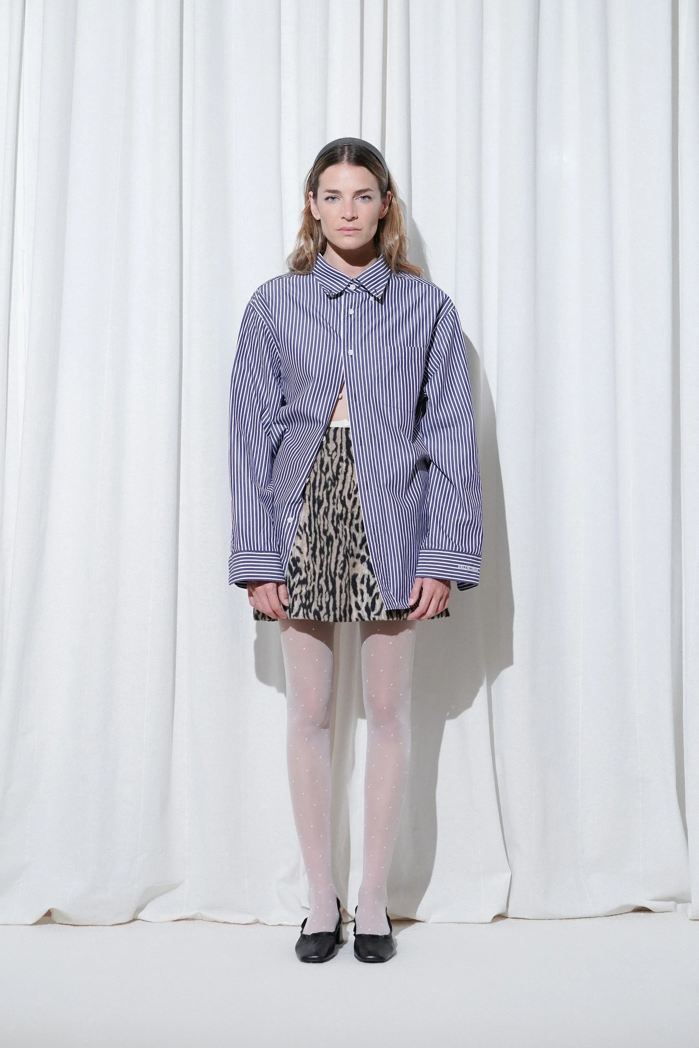 Model in an elegant layered outfit with a long black tailored coat and burgundy bodysuit, styled with EDLA Orbit White Polka Dots Tights and EDLA Mercury Black Leather Kitten Heels.