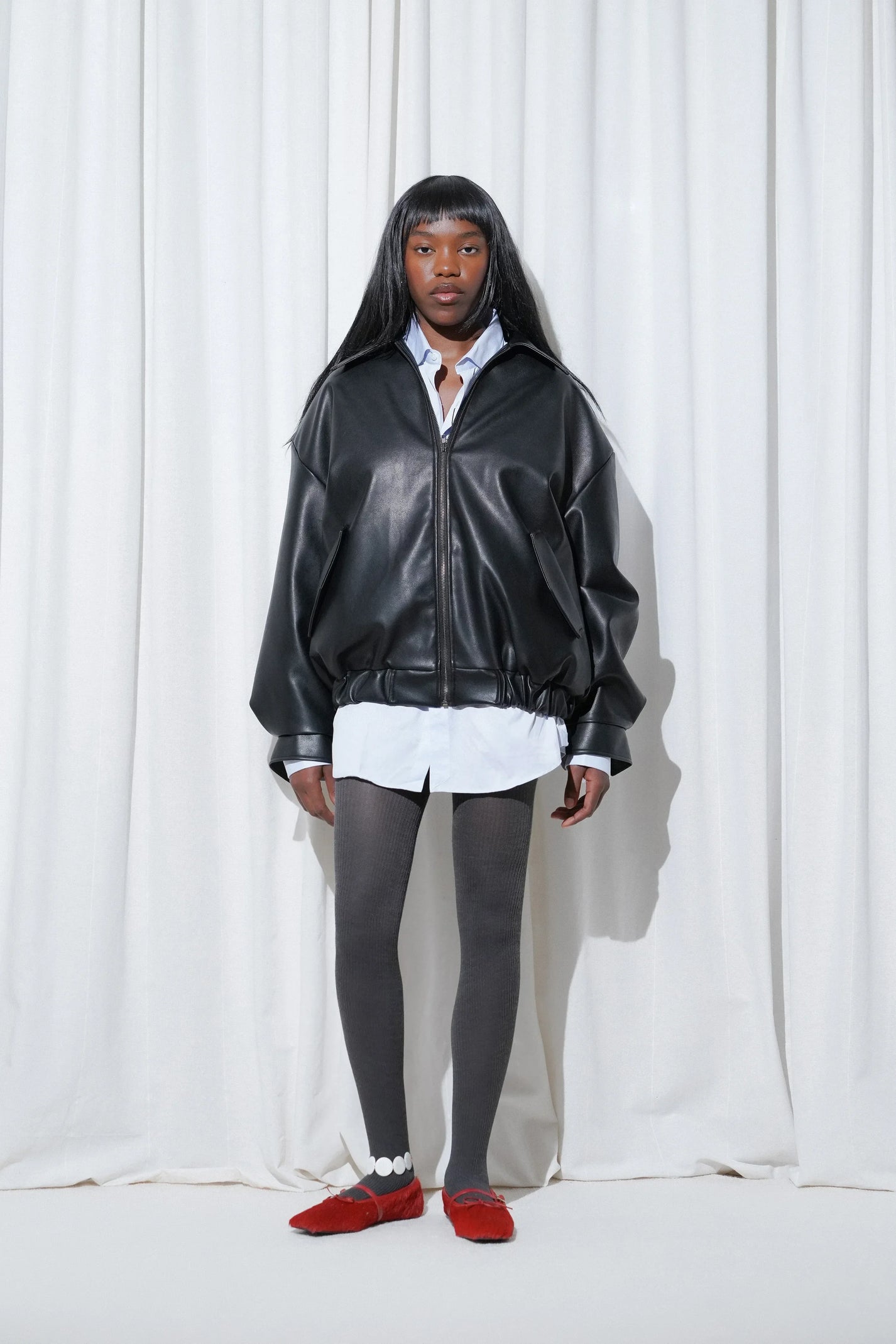 Model in an oversized black leather jacket layered over a crisp white shirt, styled with EDLA Cosmo Ribbed Wool Grey Tights and EDLA Mars Red Hair-Calf Mary-Jane Flats, balancing structured layers with a luxe textured finish.