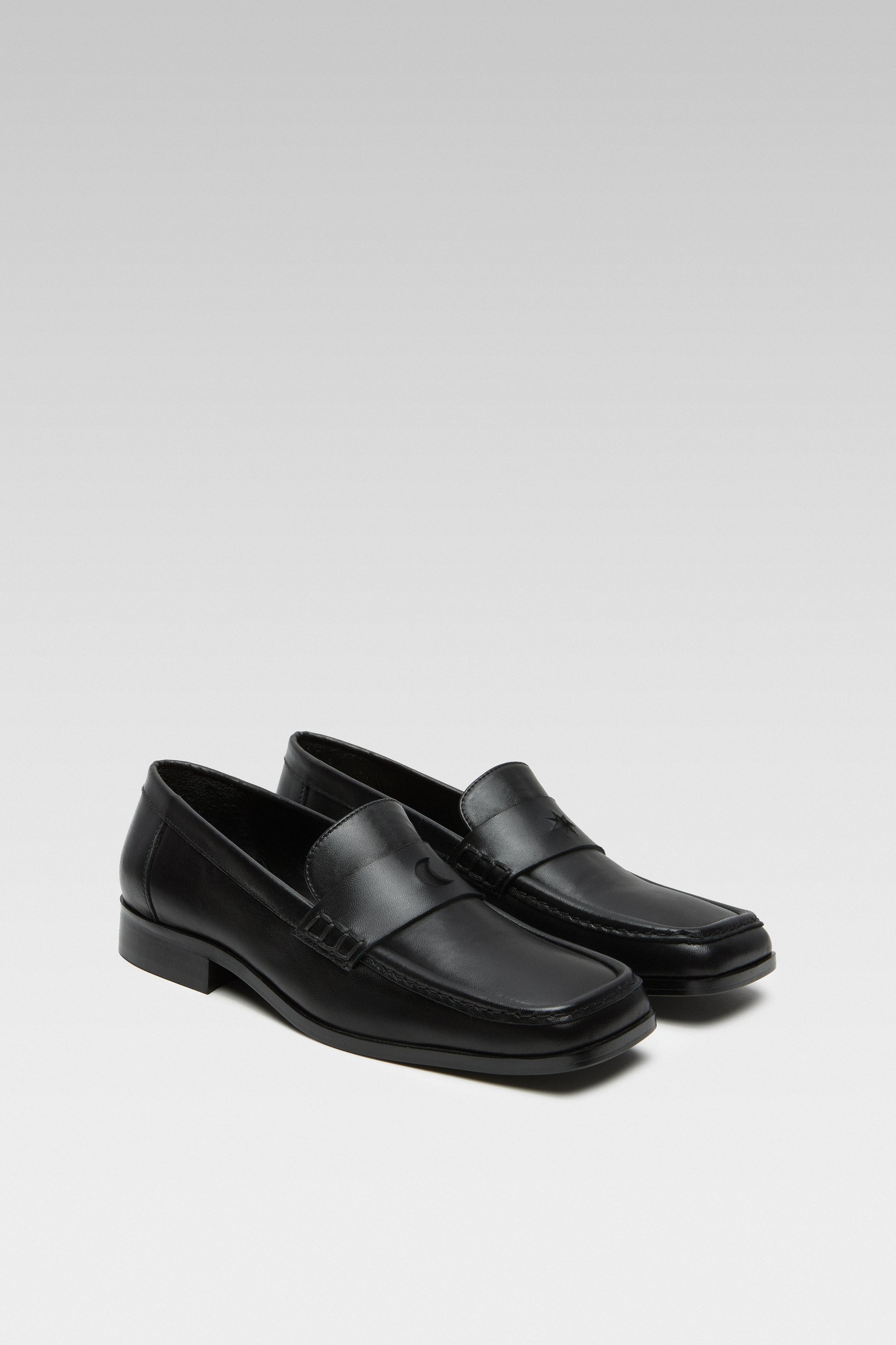 Three-quarter view of EDLA Earth black loafers for women crafted from leather with a square toe and star and moon inserts at the front.
