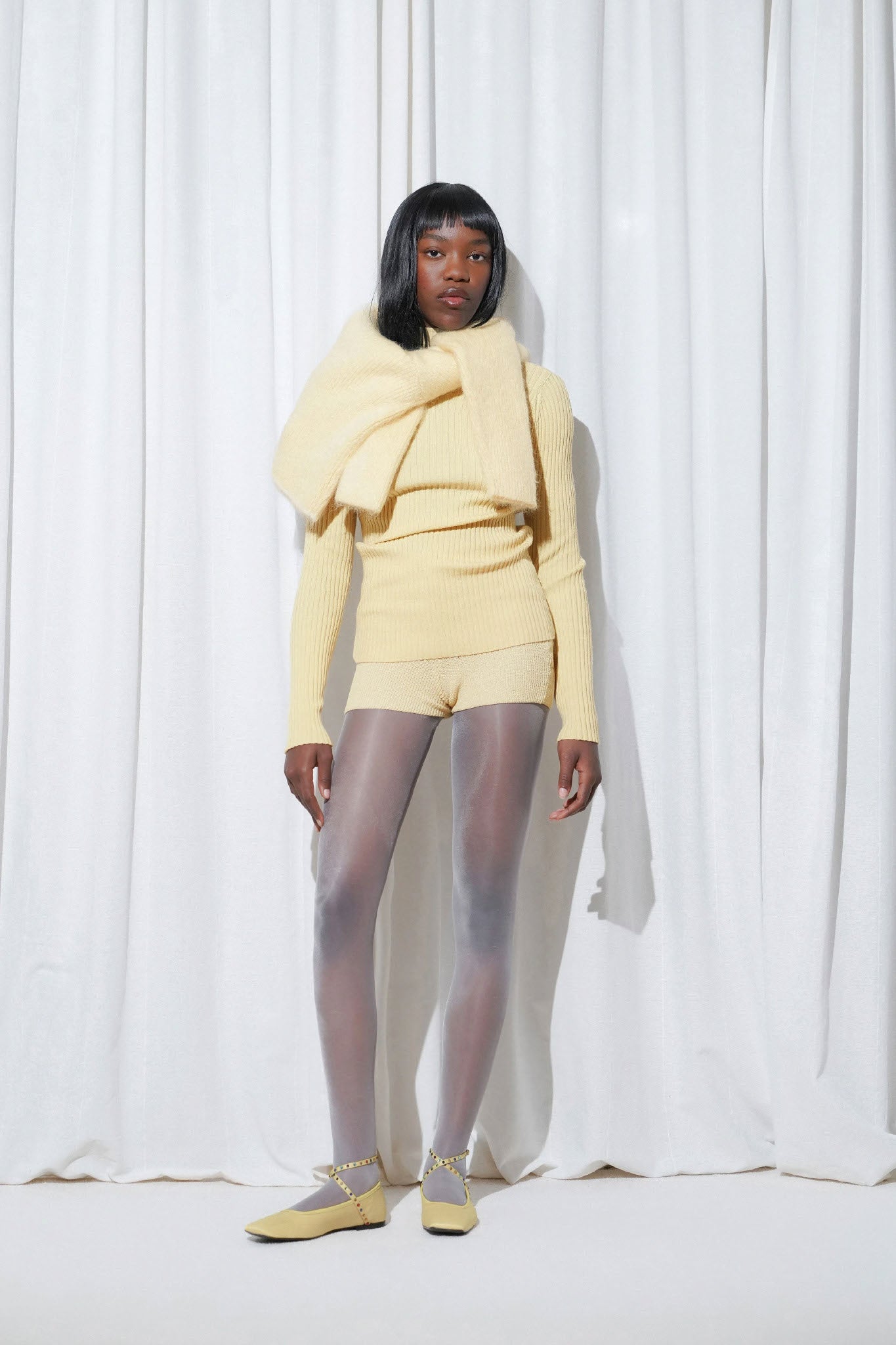 Model in a weekend outfit with yellow knit sweater, matching shorts, EDLA Galaxy Light Grey Tights, and EDLA Saturn Yellow Ballet Flats.