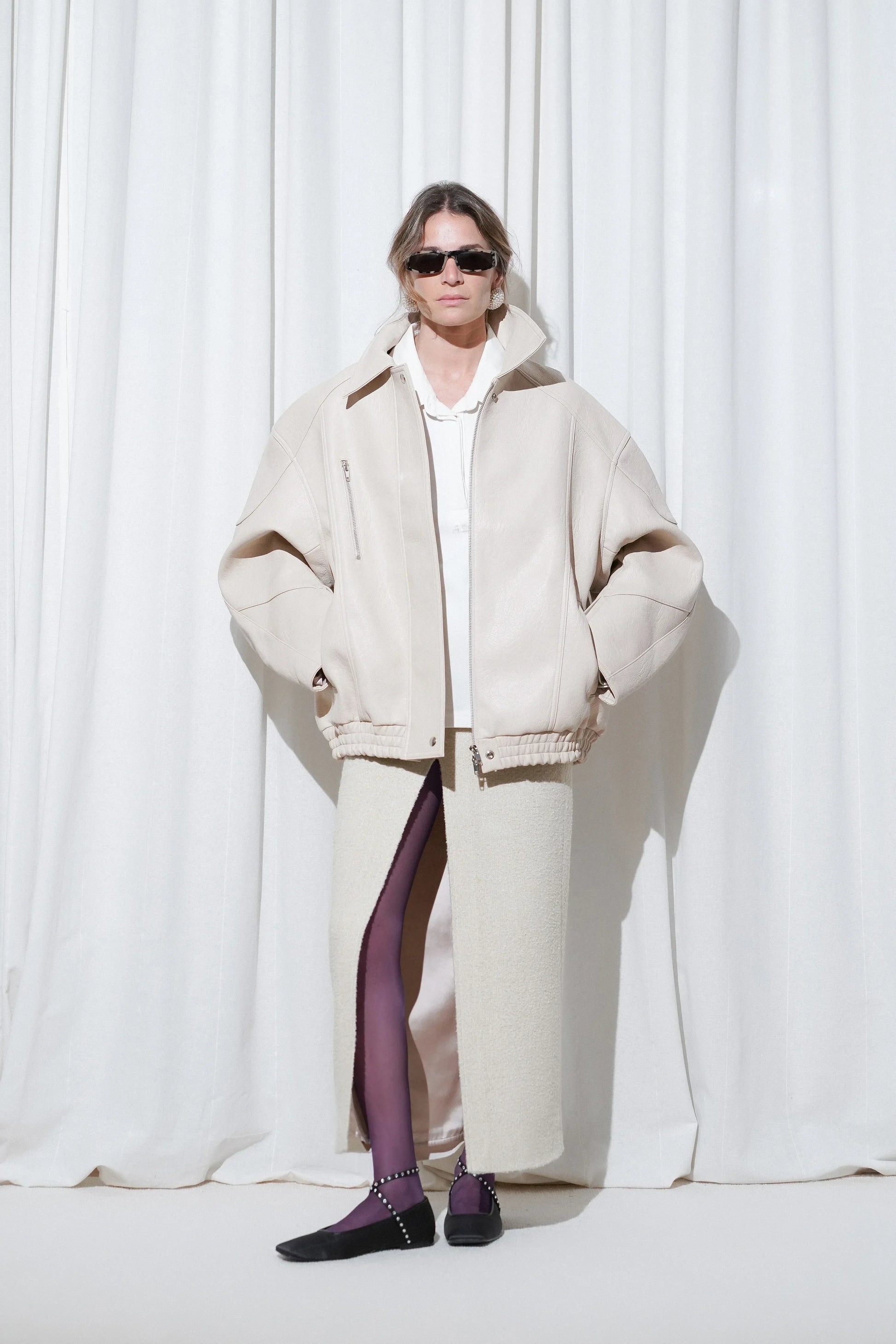 Model wearing a business casual outfit with an oversized cream bomber jacket, ivory textured midi skirt with side slit, EDLA Galaxy Purple Tights, and EDLA Saturn Black Ballet Flats.