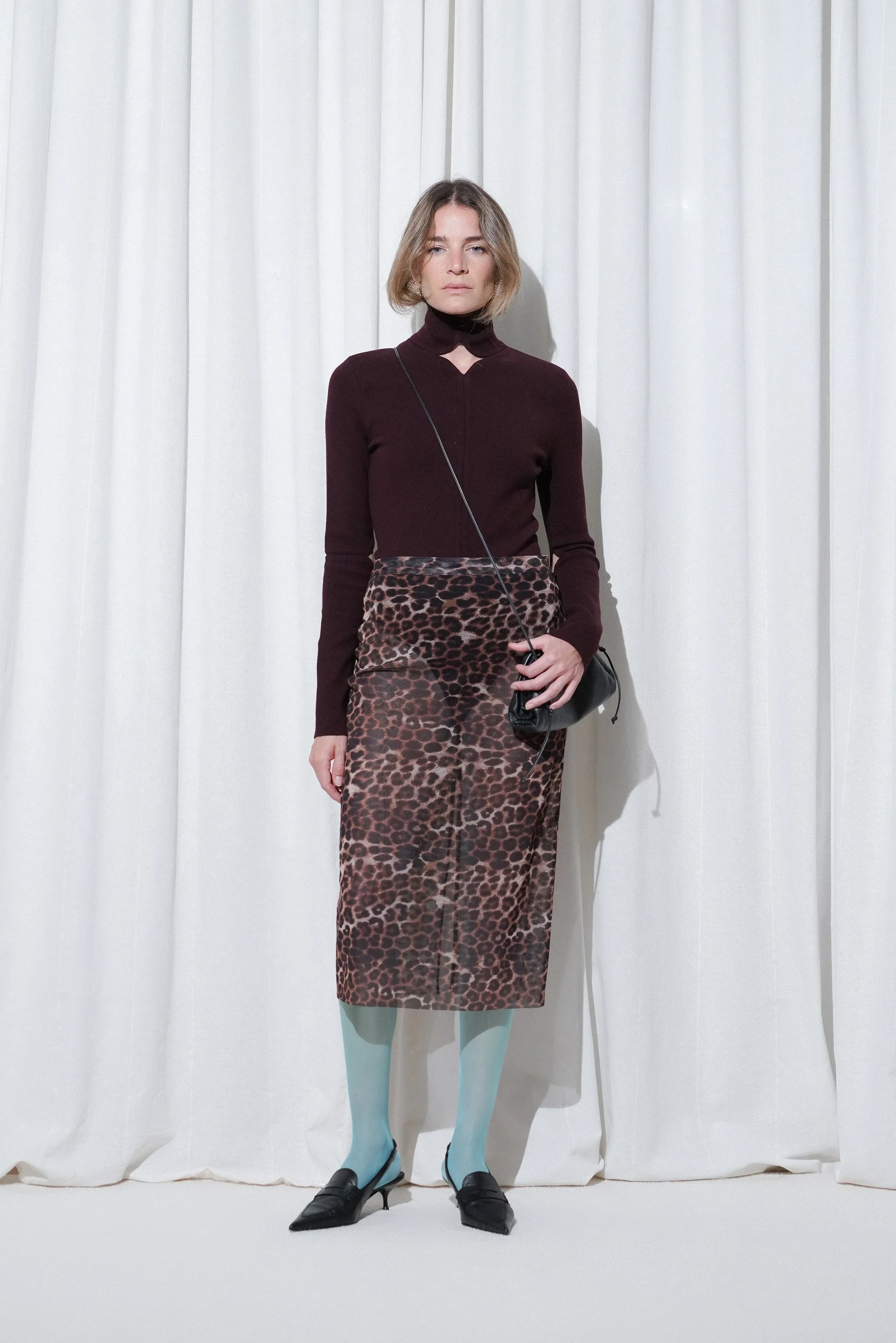 Model wearing a chic nightout look with a burgundy cutout knit top, leopard print midi skirt, EDLA Galaxy Aquamarine Tights, and EDLA Uranus Black Slingbacks.