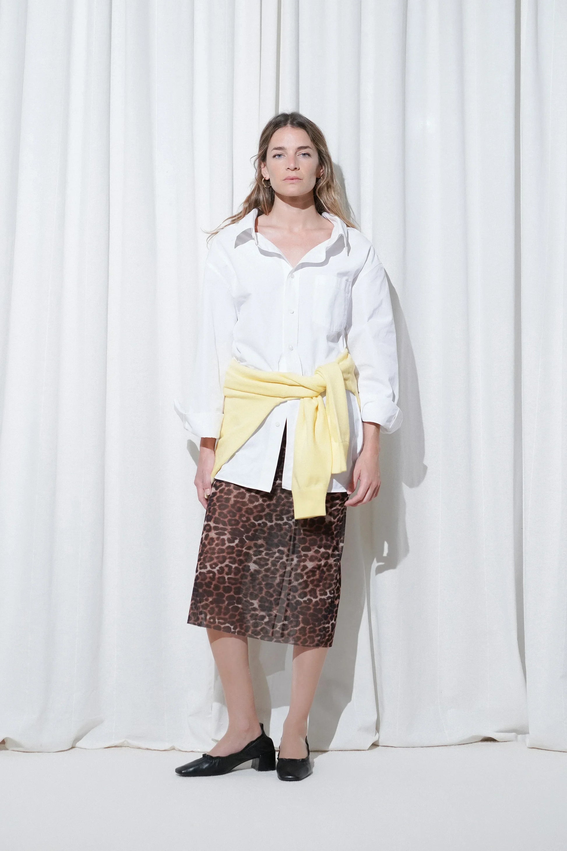 Model in a weekend outfit with oversized white shirt, yellow sweater, leopard print midi skirt, EDLA Eclipse Nude Tights and EDLA Mercury Black Kitten Heels.
