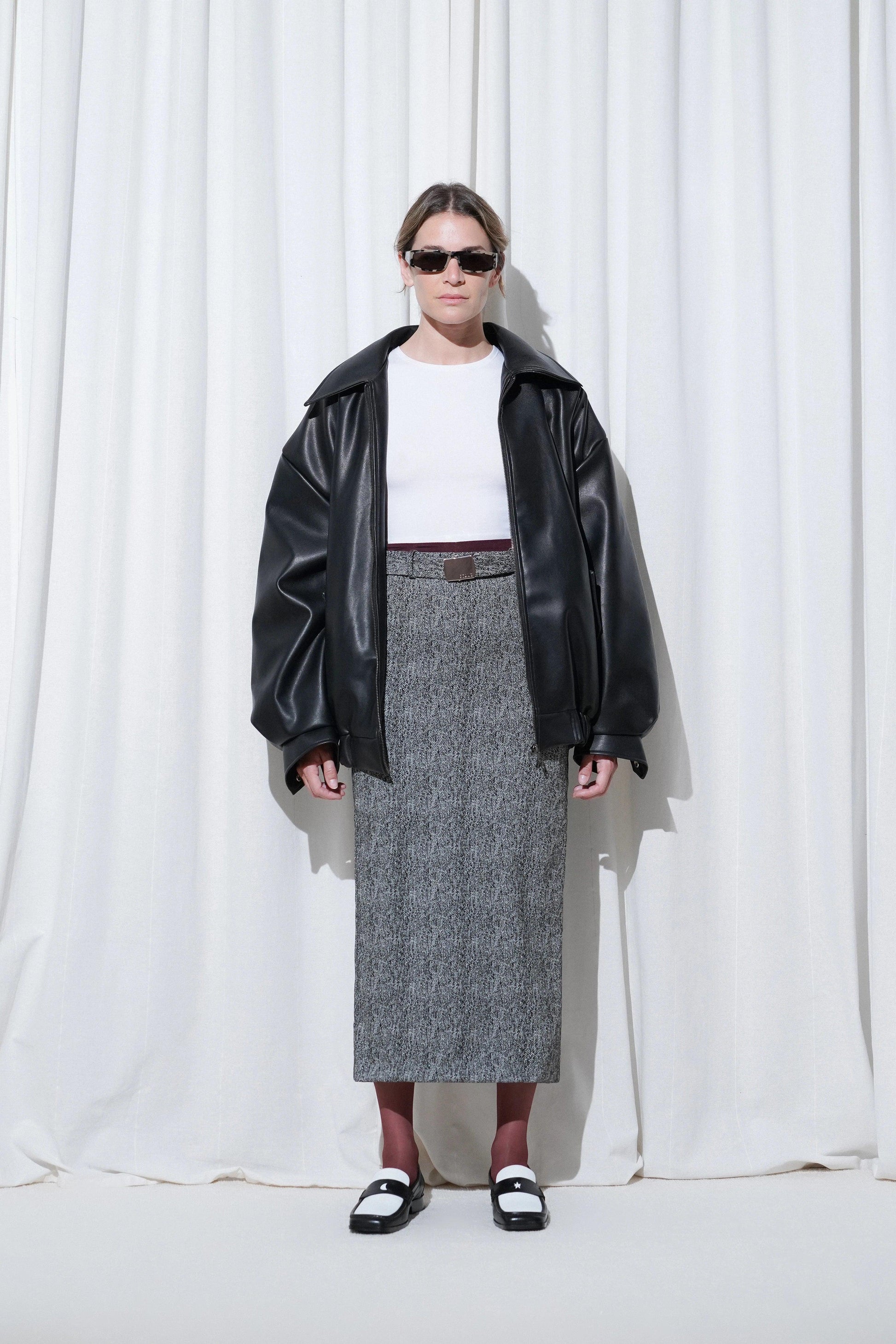 Model in a casual business outfit with black oversized leather jacket, white t-shirt, grey midi skirt, EDLA Galaxy Burgundy Tights and EDLA Earth Black and White Loafers.