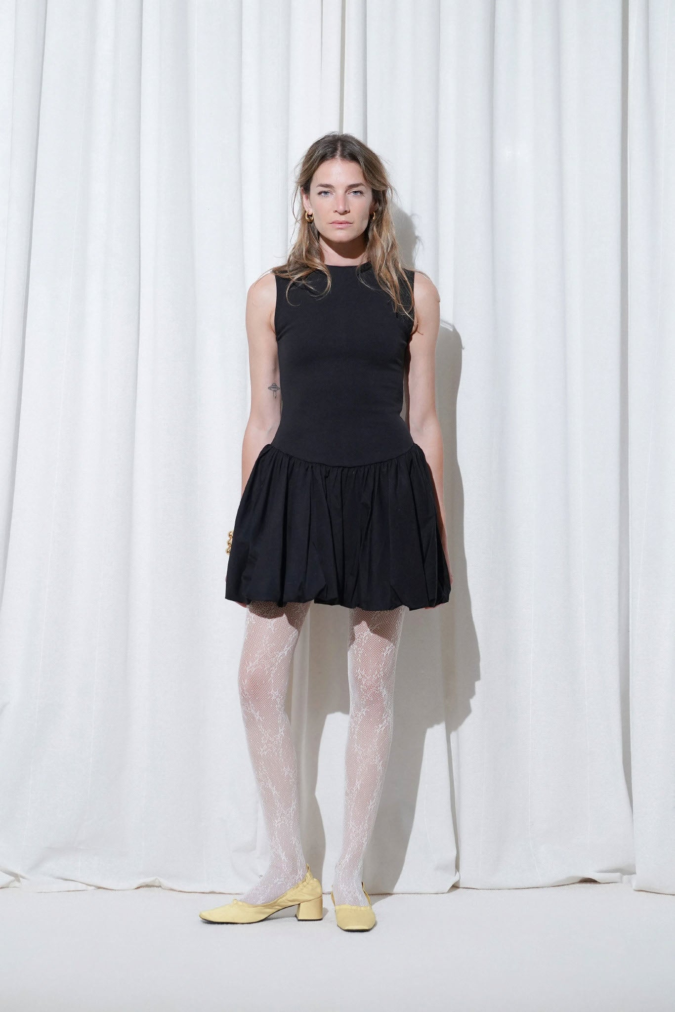 Model in a chic black sleeveless mini dress styled with EDLA Starlight White Tights and EDLA Mercury Yellow Kitten Heels, creating a bold monochrome contrast with a playful pop of color.