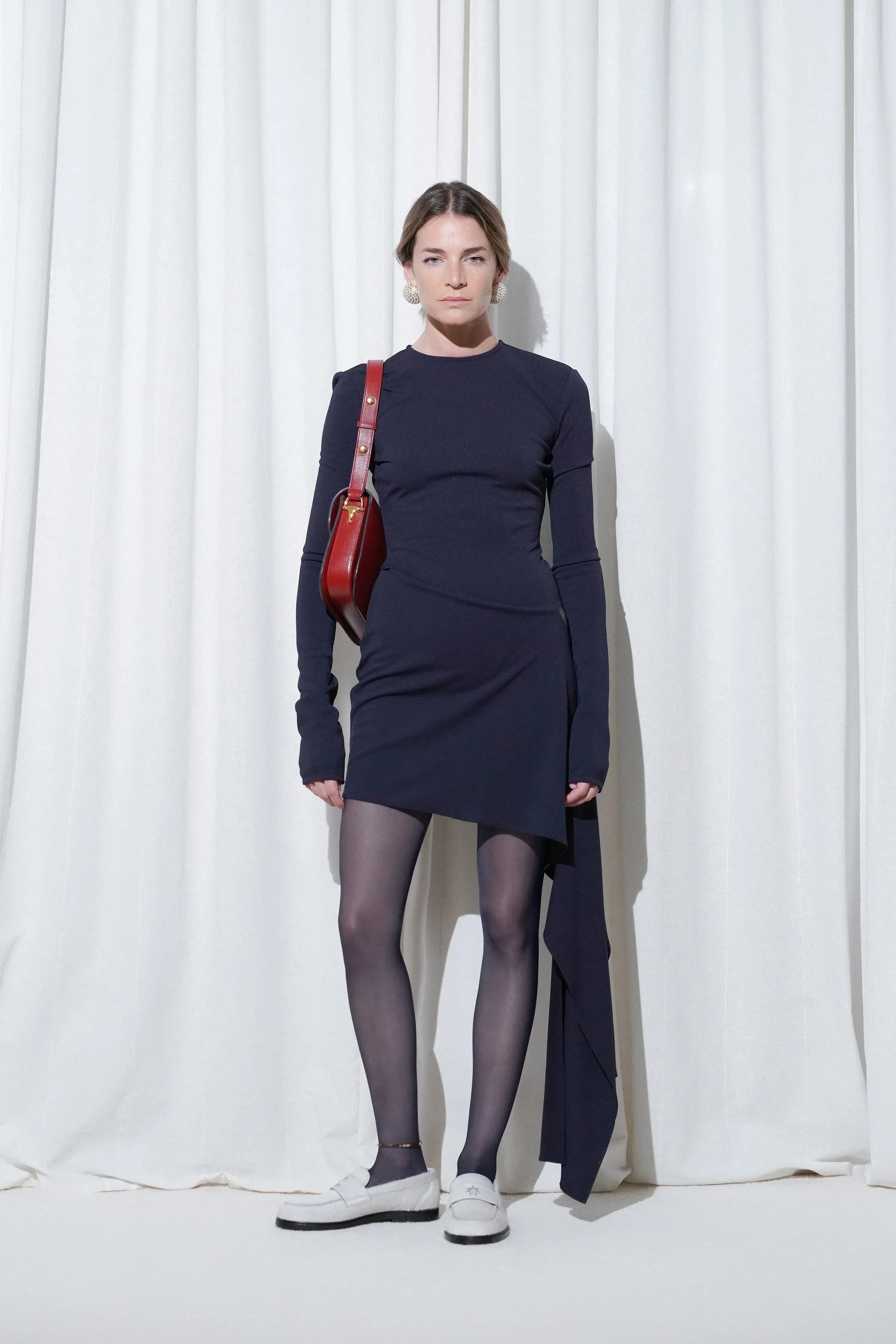 Model in a party outfit with navy asymmetric dress, red shoulder bag, gold anklet, EDLA Galaxy Navy Tights, and EDLA Jupiter White Loafers.