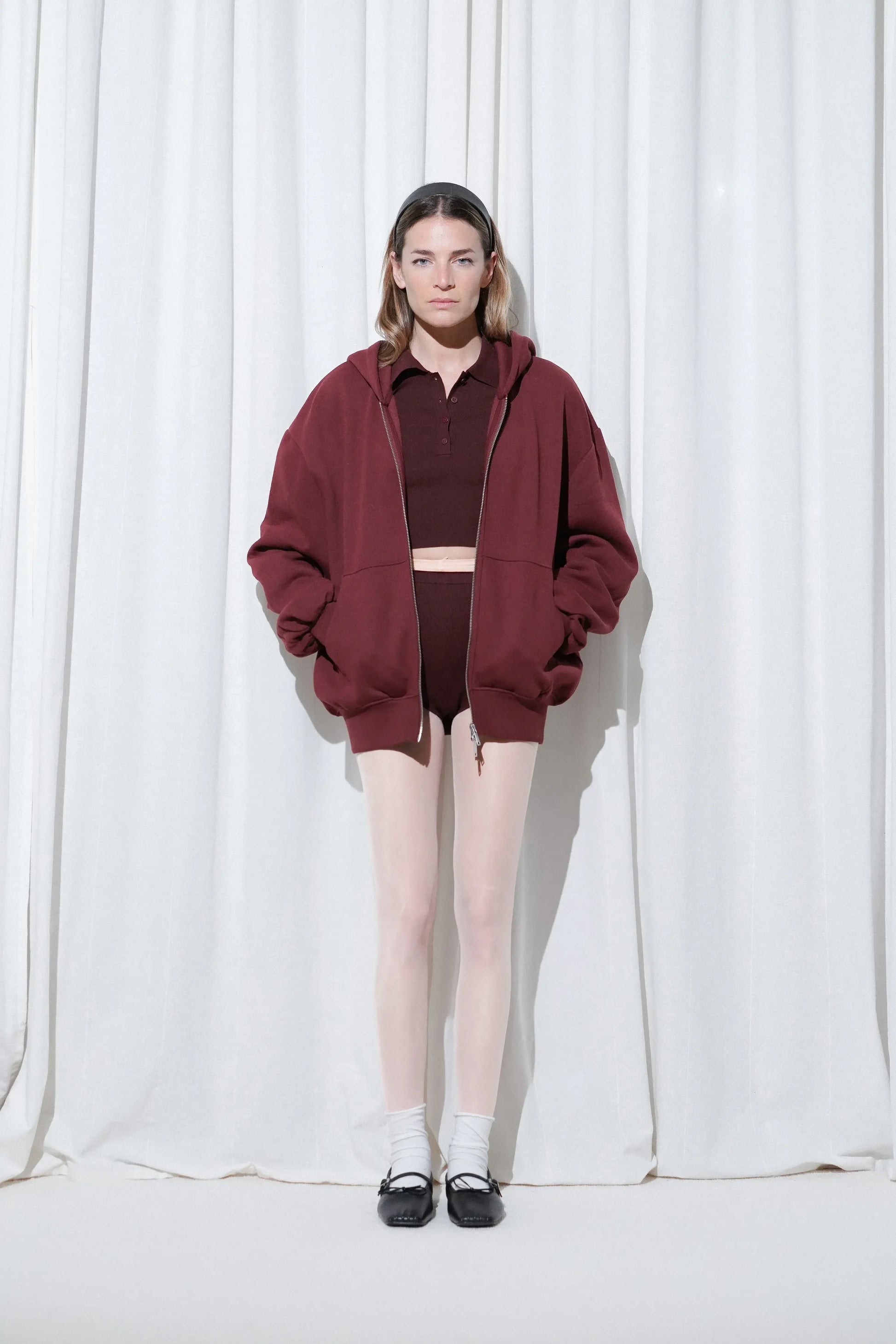 Model wearing a laid-back casual look with a burgundy hoodie layered over a matching burgundy cropped polo and shorts, styled with EDLA Galaxy PaLE Pink Tights, EDLA Ursa White socks, and EDLA Mars Black Ballet Flats.