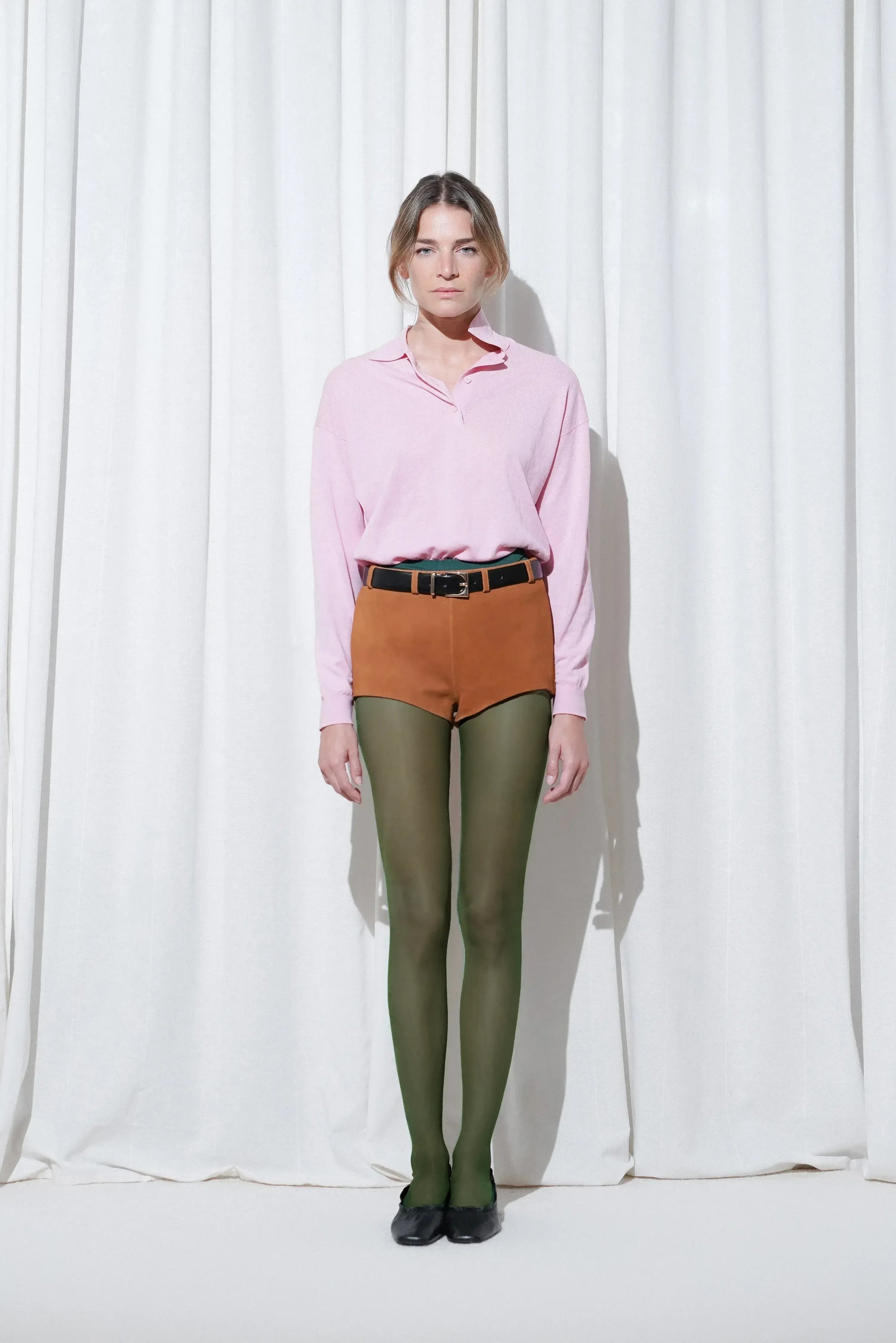 Model in a weekend outfit with pink long-sleeve polo, brown suede shorts, EDLA Galaxy Dark Green Tights, and EDLA Mercury Black Kitten Heels.