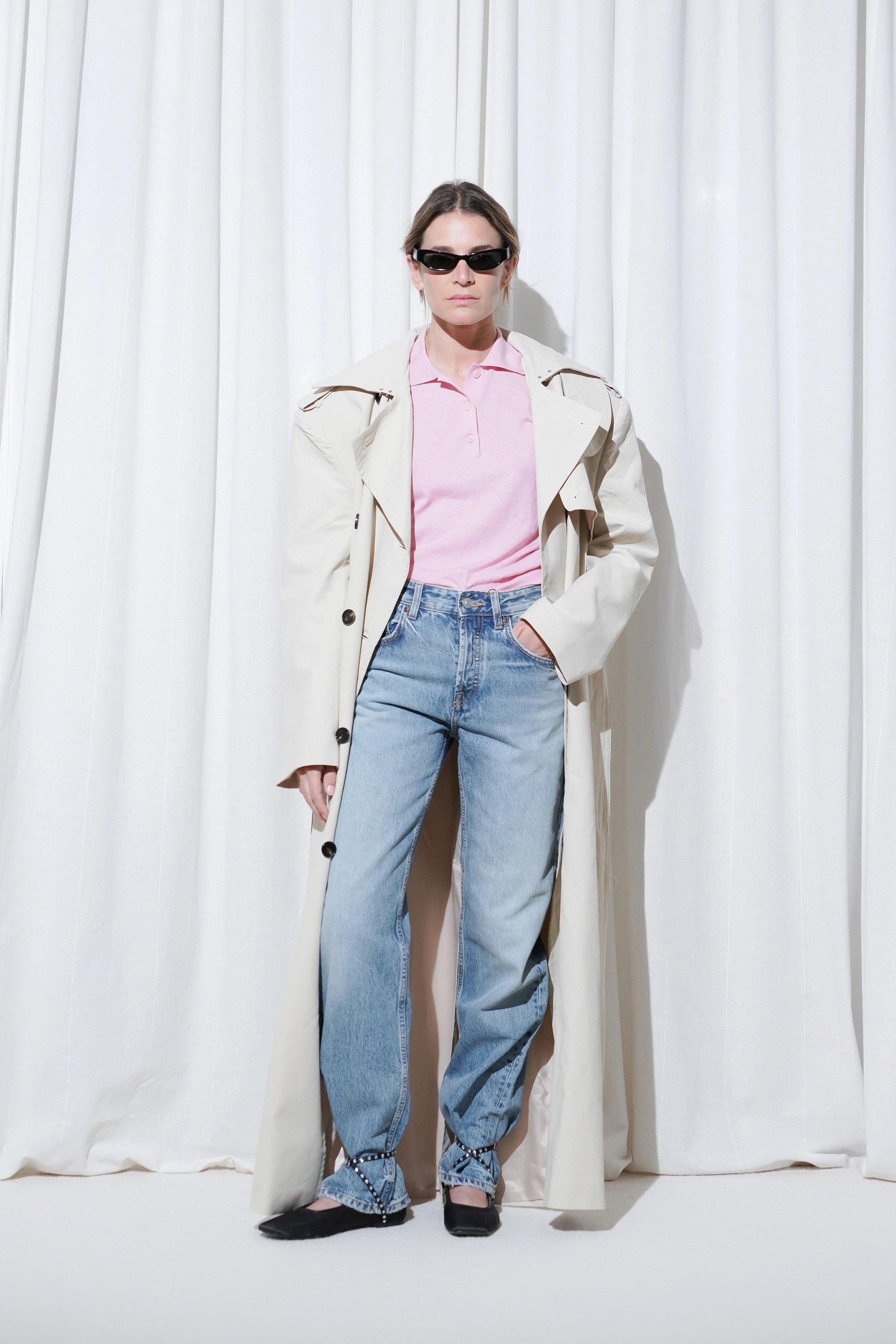Model in a weekend outfit with beige trench coat, pink polo shirt, blue jeans, and EDLA Saturn Black Ballet Flats.