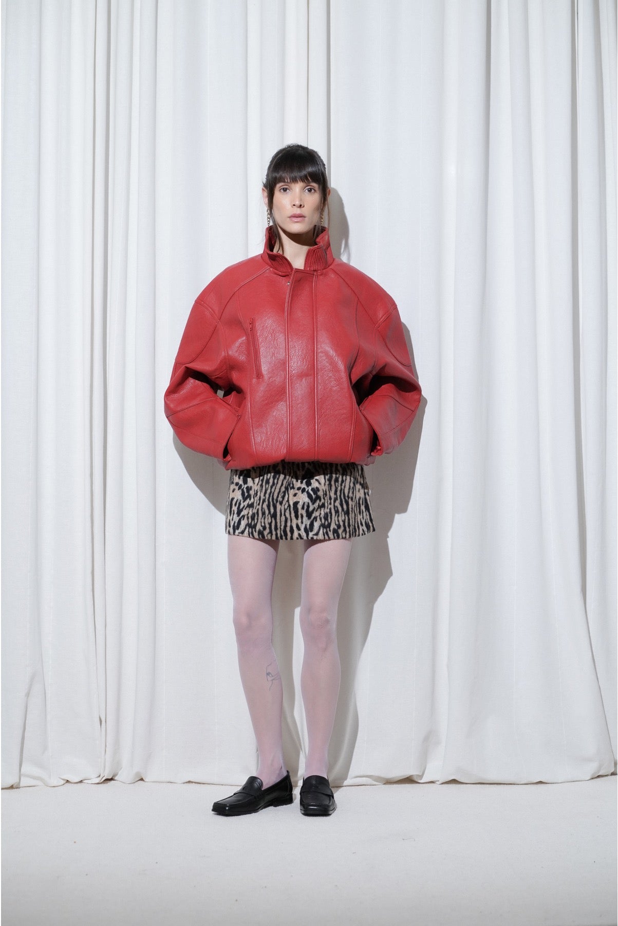 Model wearing a casual weekend Y2K outfit with an oversized red leather jacket, leopard-print mini skirt, EDLA Galaxy Lilac Tights, and EDLA Earth Black Loafers.