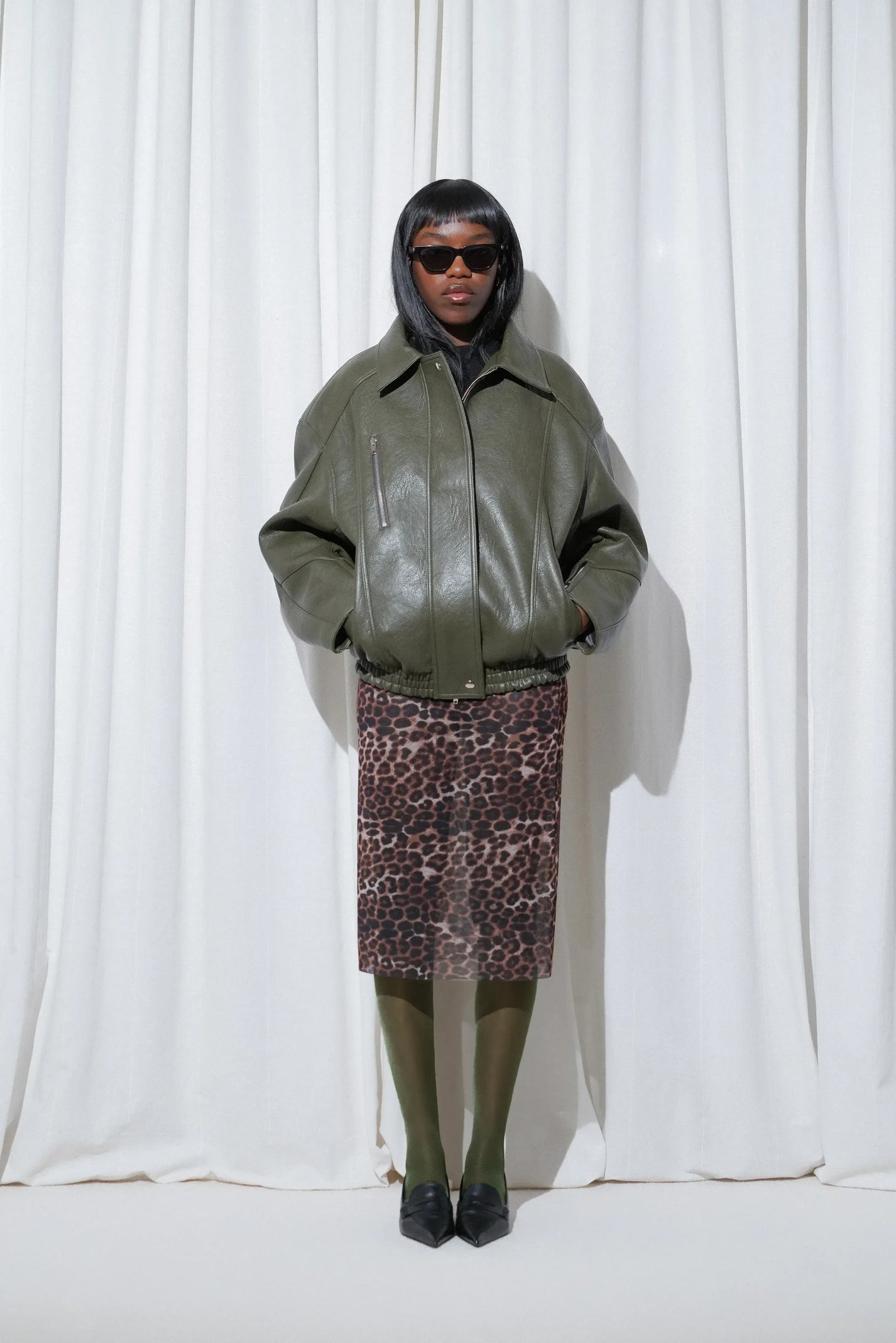 Model wearing a business casual outfit with an oversized khaki green leather jacket, leopard print midi skirt, EDLA Galaxy Dark Green Tights and EDLA Uranus Black Slingbacks.