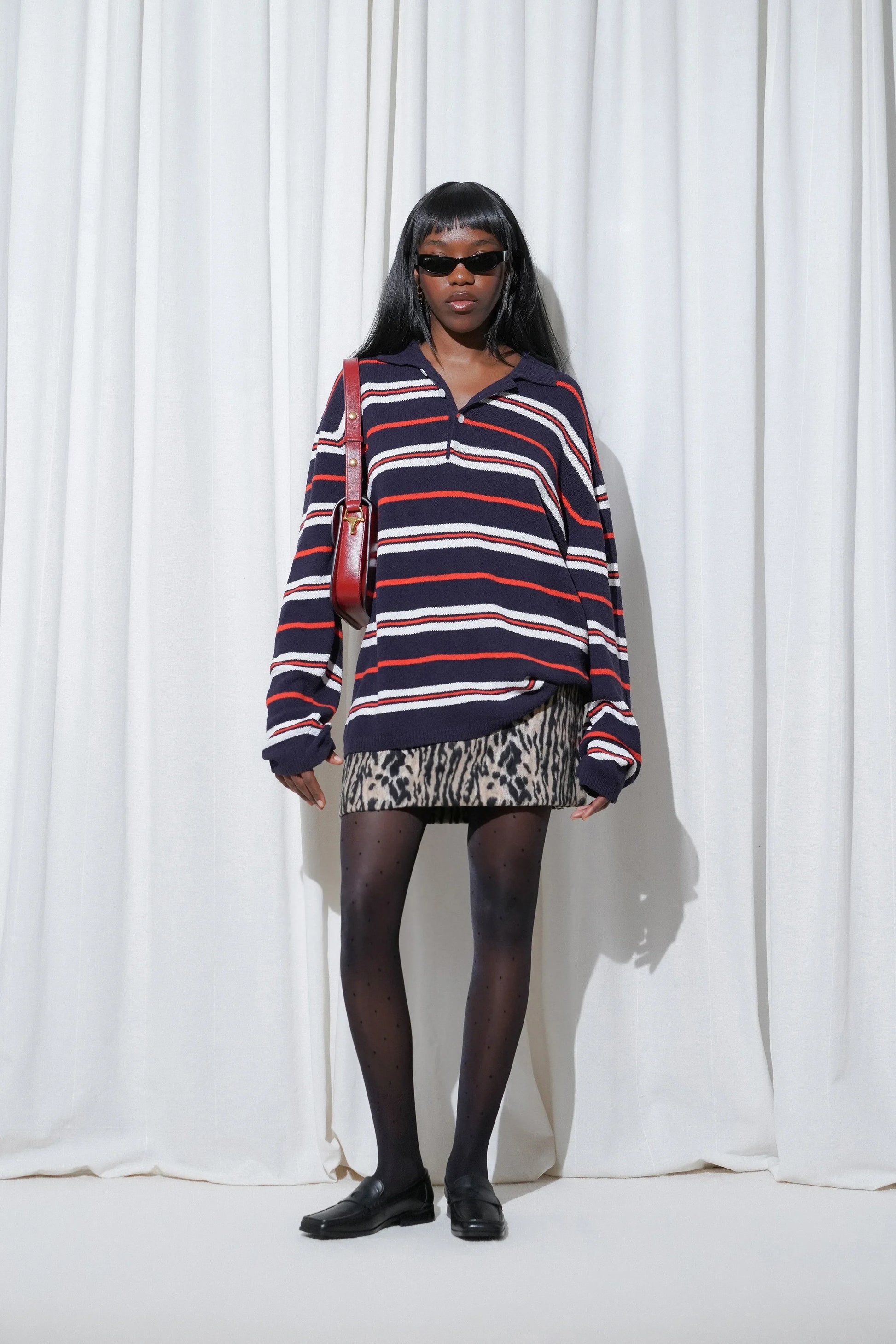 Model in a bold streetwear-inspired outfit styled with EDLA Orbit Black Polka Dots Tights and EDLA Earth Black Loafers, paired with a striped oversized sweater and leopard print mini skirt.