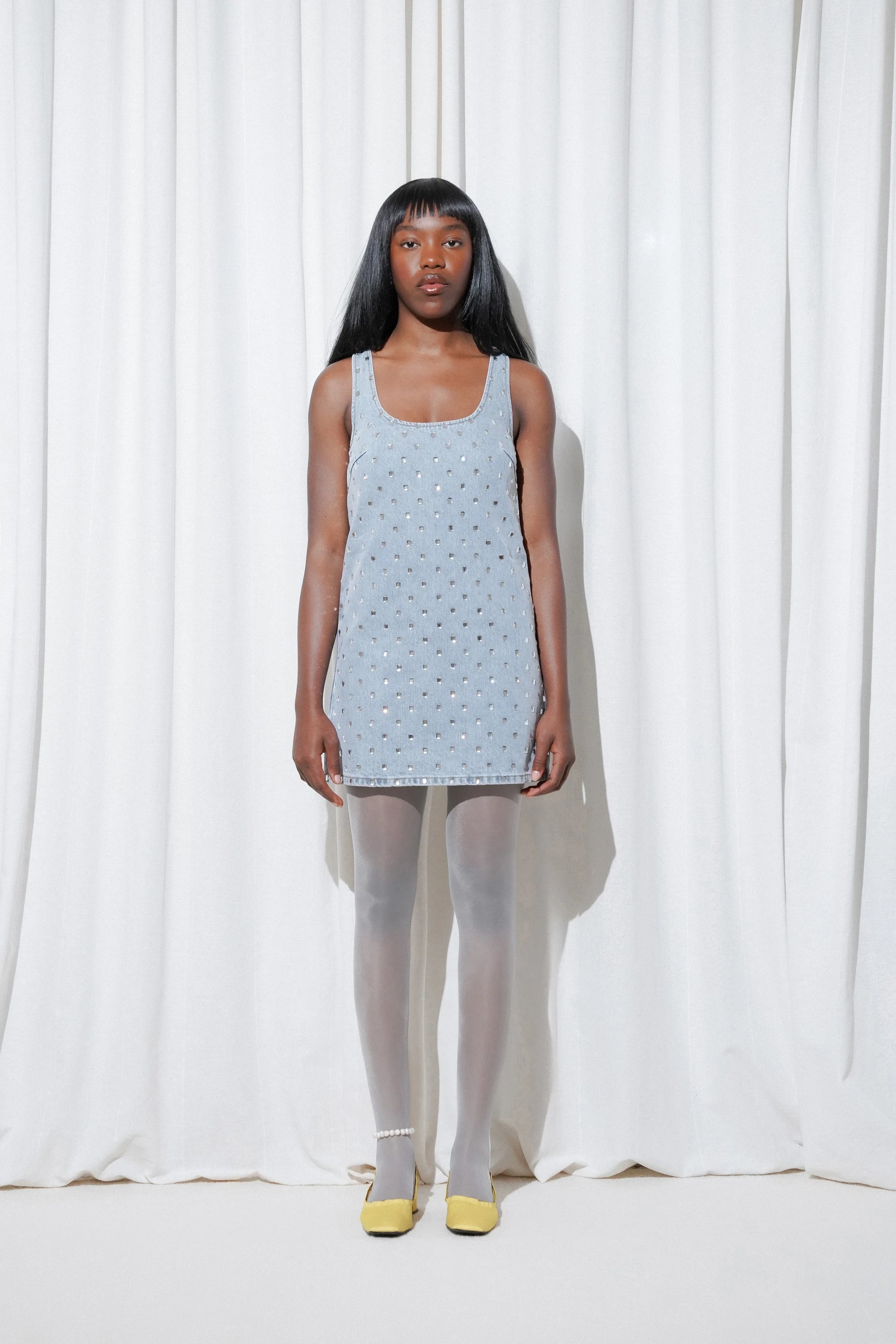 Model wearing a sparkling night-out look with a crystal-embellished mini dress, styled with pearls anklet, EDLA Galaxy Light Grey Tights and EDLA Mercury Yellow Kitten Heels.