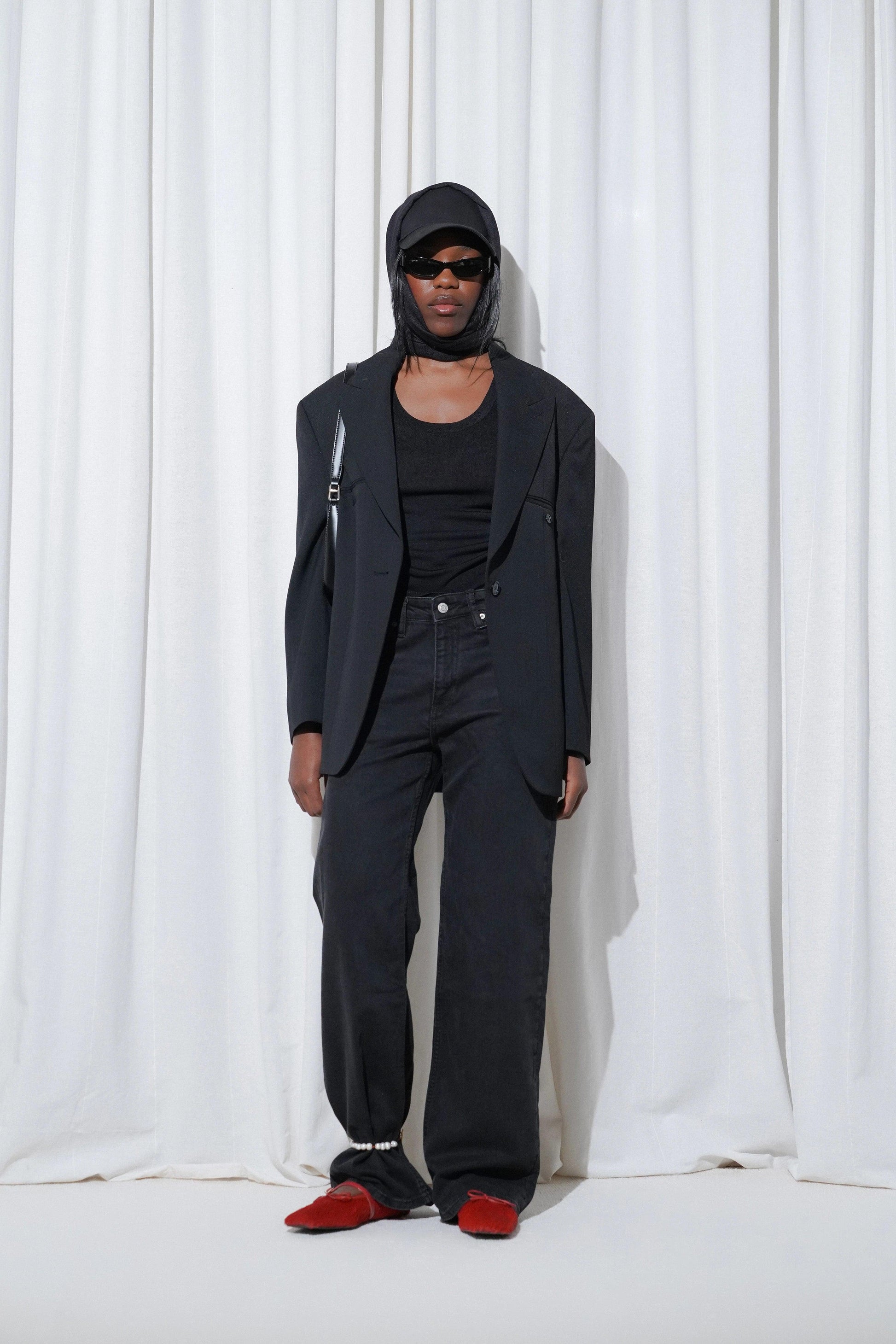 Model in a casual outfit with black blazer, tank top, black jeans, pearls anklet, cap, and EDLA Mars Red Ballet Flats.