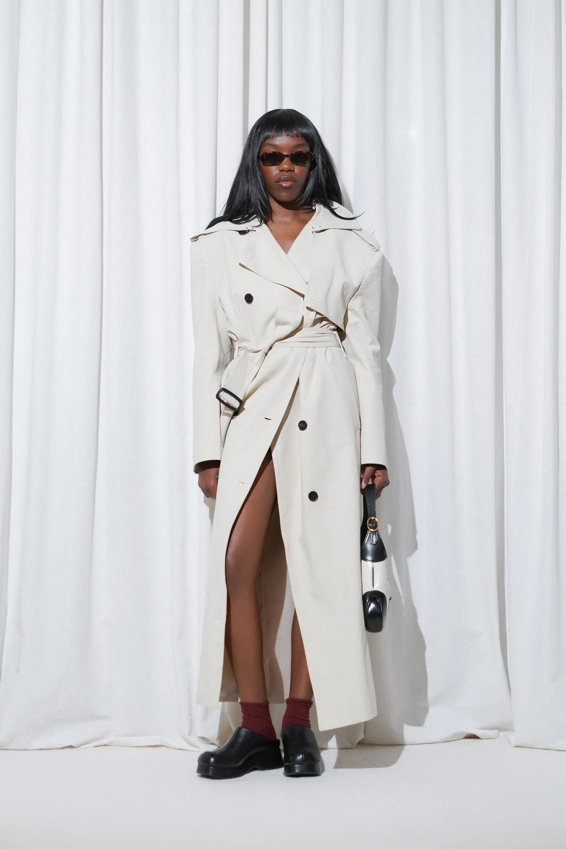 Model in a chic trench coat look styled with EDLA Burgundy Ursa Socks and EDLA Venus Black Mules, accessorized with a structured handbag and sleek sunglasses.