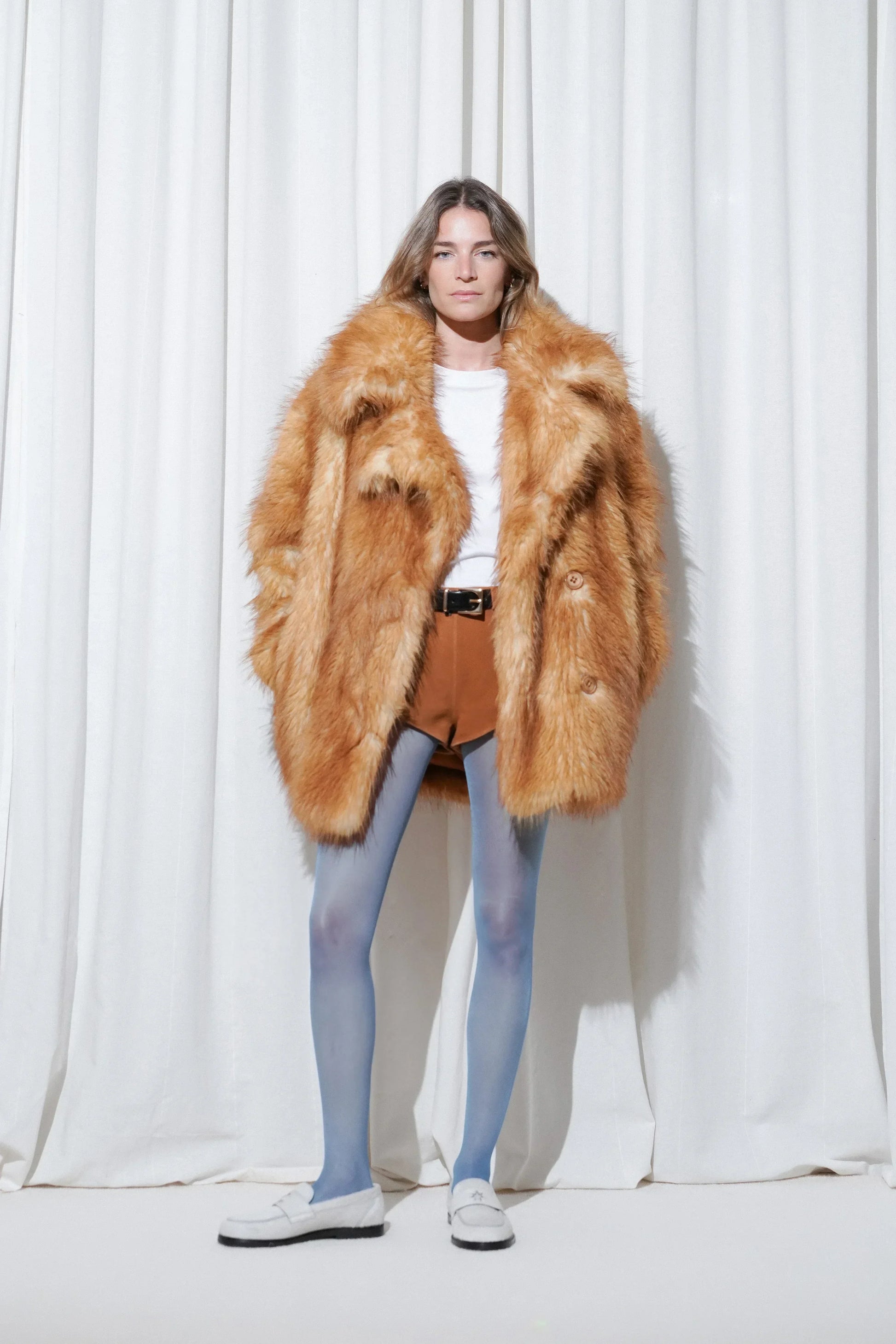 Model in a dinner outfit with brown faux fur coat, white t-shirt, brown suede shorts, EDLA Galaxy Blue Tights, and EDLA Jupiter White Loafers.