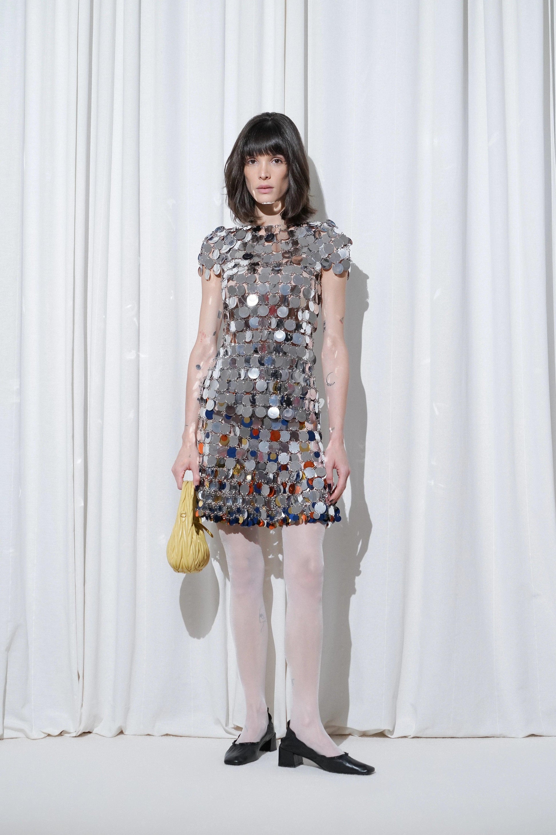 Model wearing a dazzling night-out outfit with a mirrored disc sequins matching top and skirt, styled with EDLA Galaxy White Tights and EDLA Uranus Black Slingbacks.