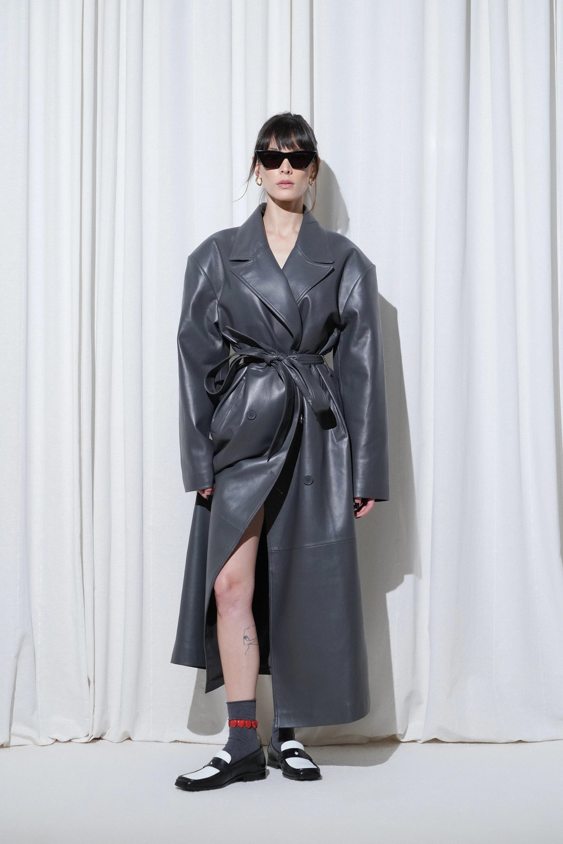 Model in a weekend outfit with oversized grey leather trench coat, hearts anklet, EDLA Ursa Grey Socks, and EDLA Earth Black and White Loafers.