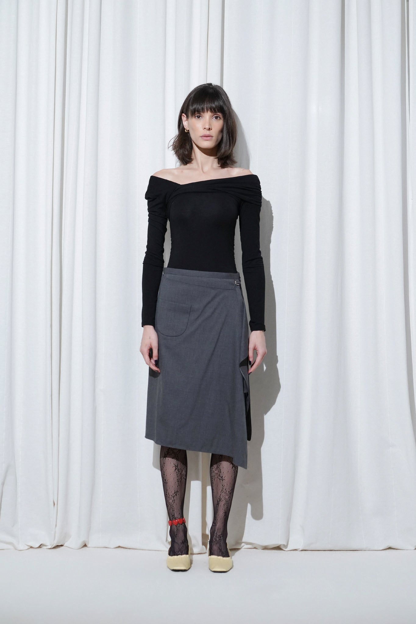 Model styled in a minimalist black off-shoulder top and grey wrap skirt, paired with EDLA Starlight Black Tights and EDLA Mercury Yellow Kitten Heels for a chic yet playful contrast.