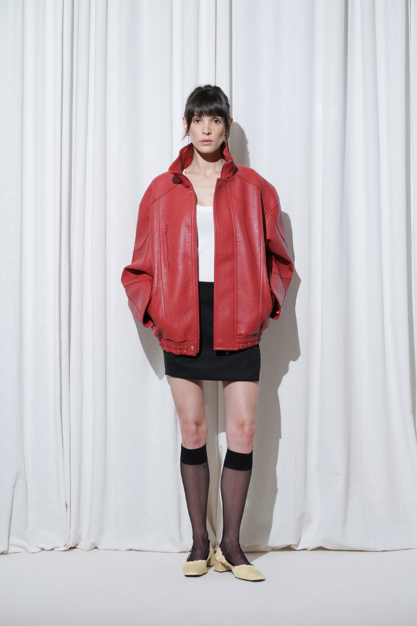 Model in a Y2K outfit with oversized red leather jacket, mini black skirt, EDLA Stellar Knee High Socks and EDLA Mercury Yellow Kitten Heels.