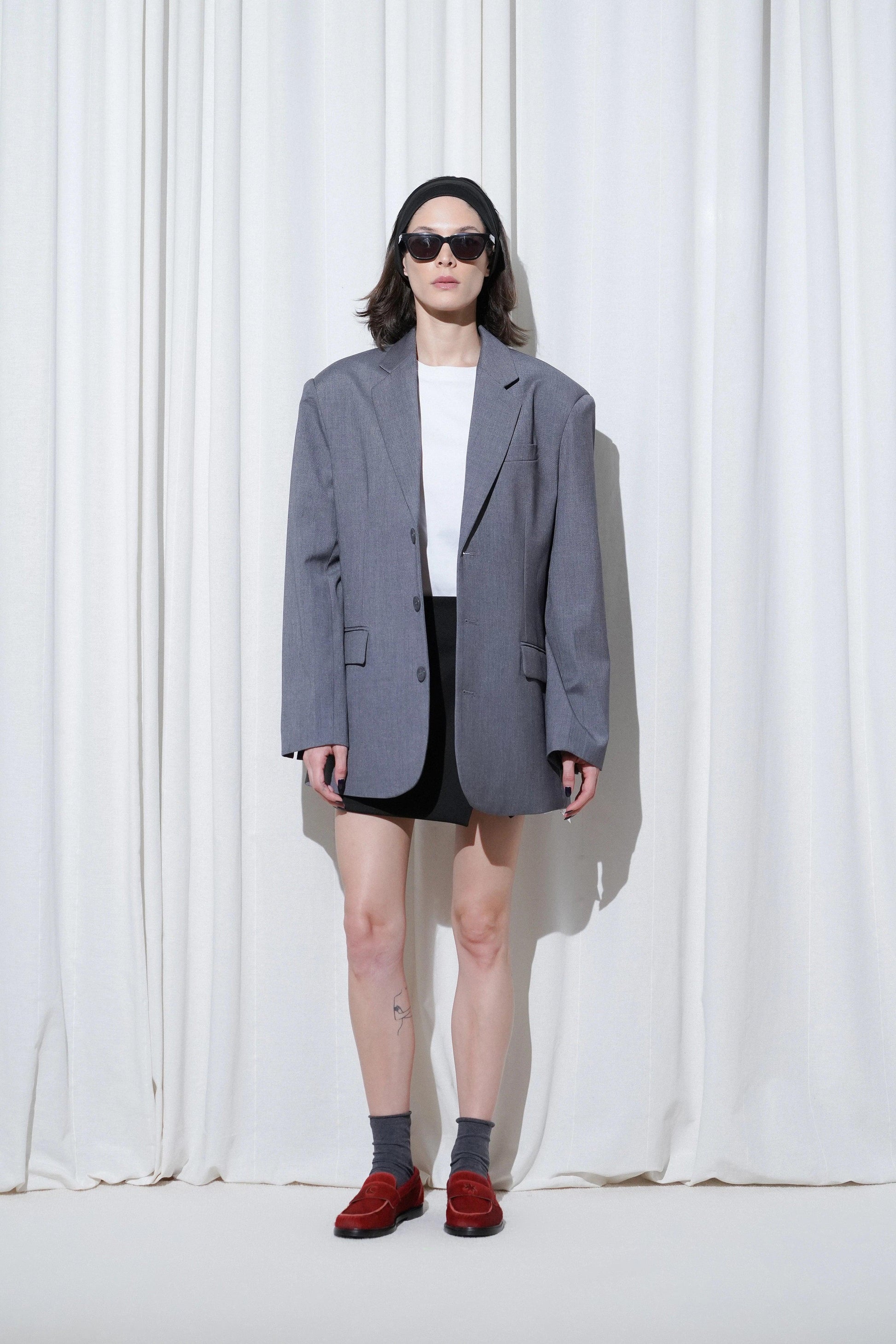 Model in a casual business outfit with oversized grey blazer, white t-shirt, black mini skirt, and EDLA Jupiter Red Loafers.