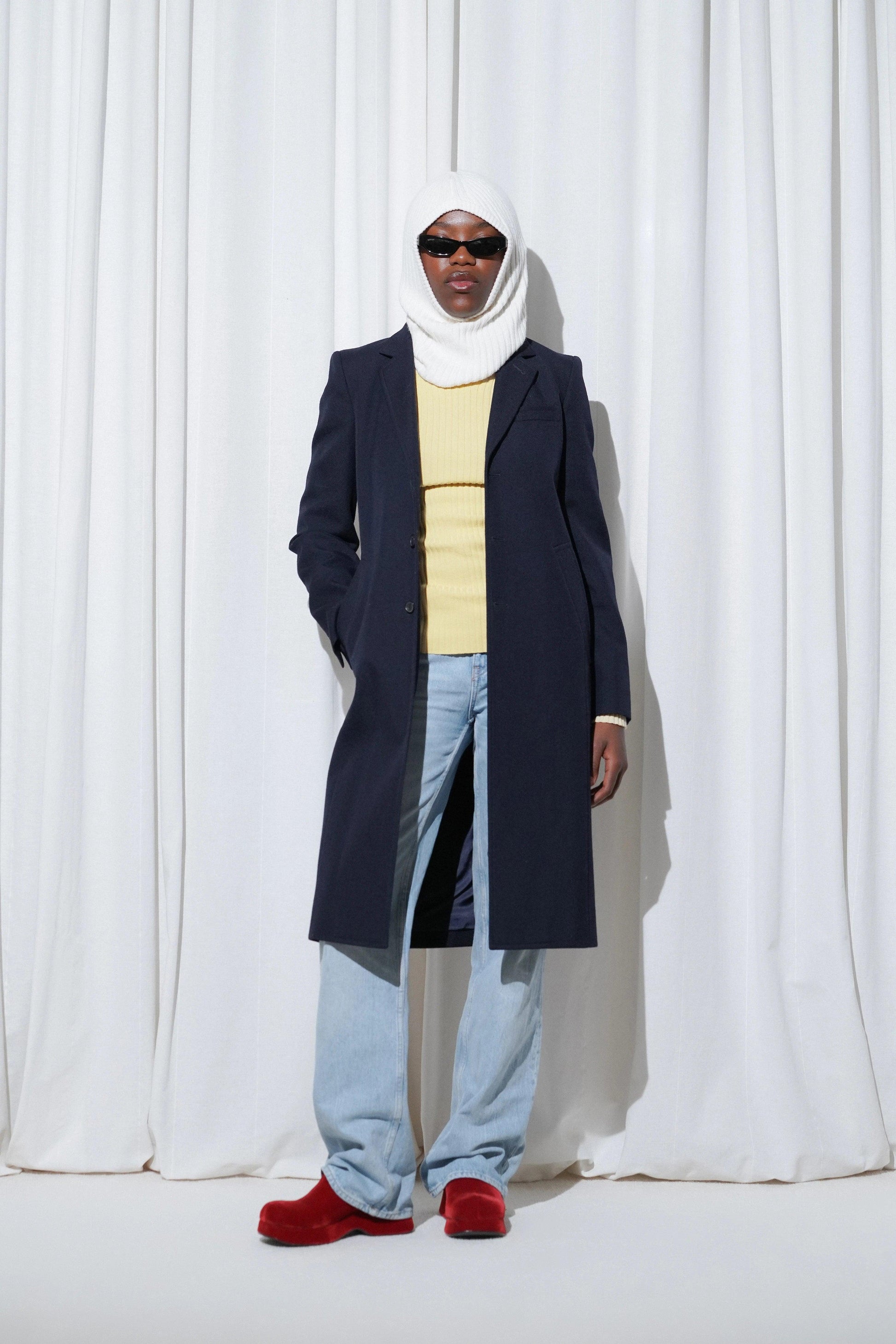 Model in an airport outfit with navy coat, yellow knit, light jeans, and EDLA Venus Burgundy Mules.