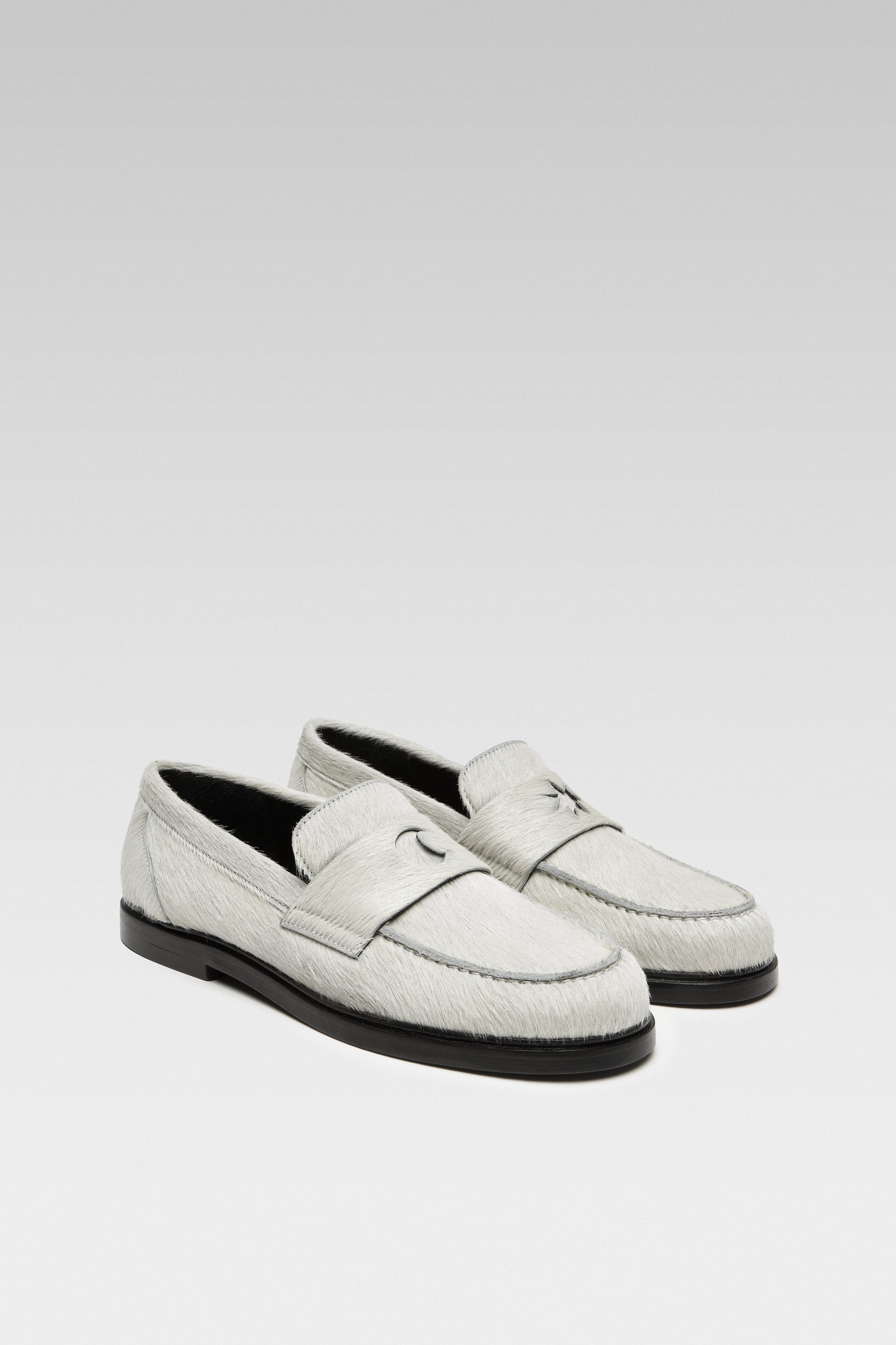 Three-quarter view of EDLA Jupiter white loafers for women crafted from calf hair with a round toe and star and moon inserts at the front.