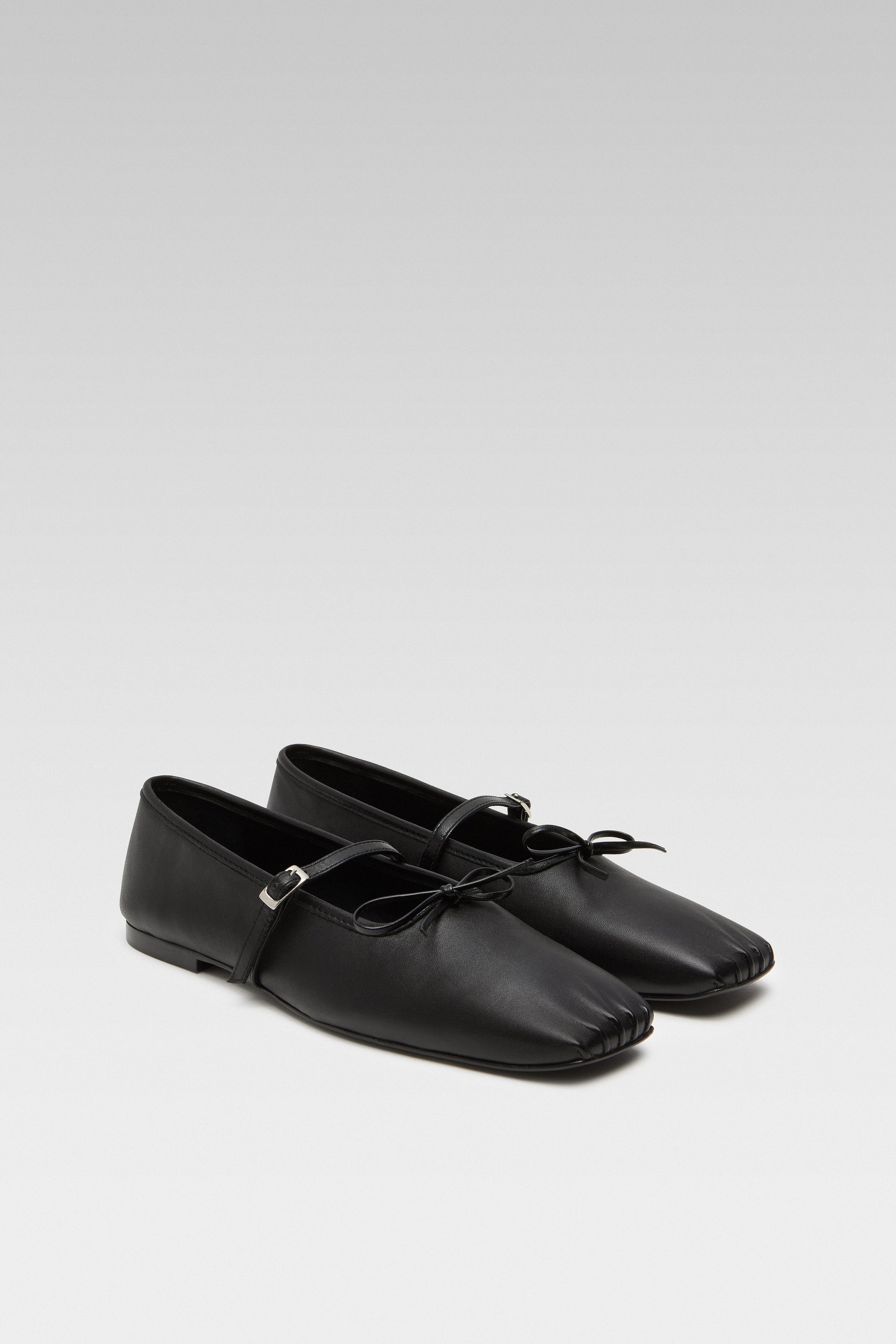 Three-quarter view of EDLA Mars black ballet flats crafted from leather with a squared toe and bow detail.