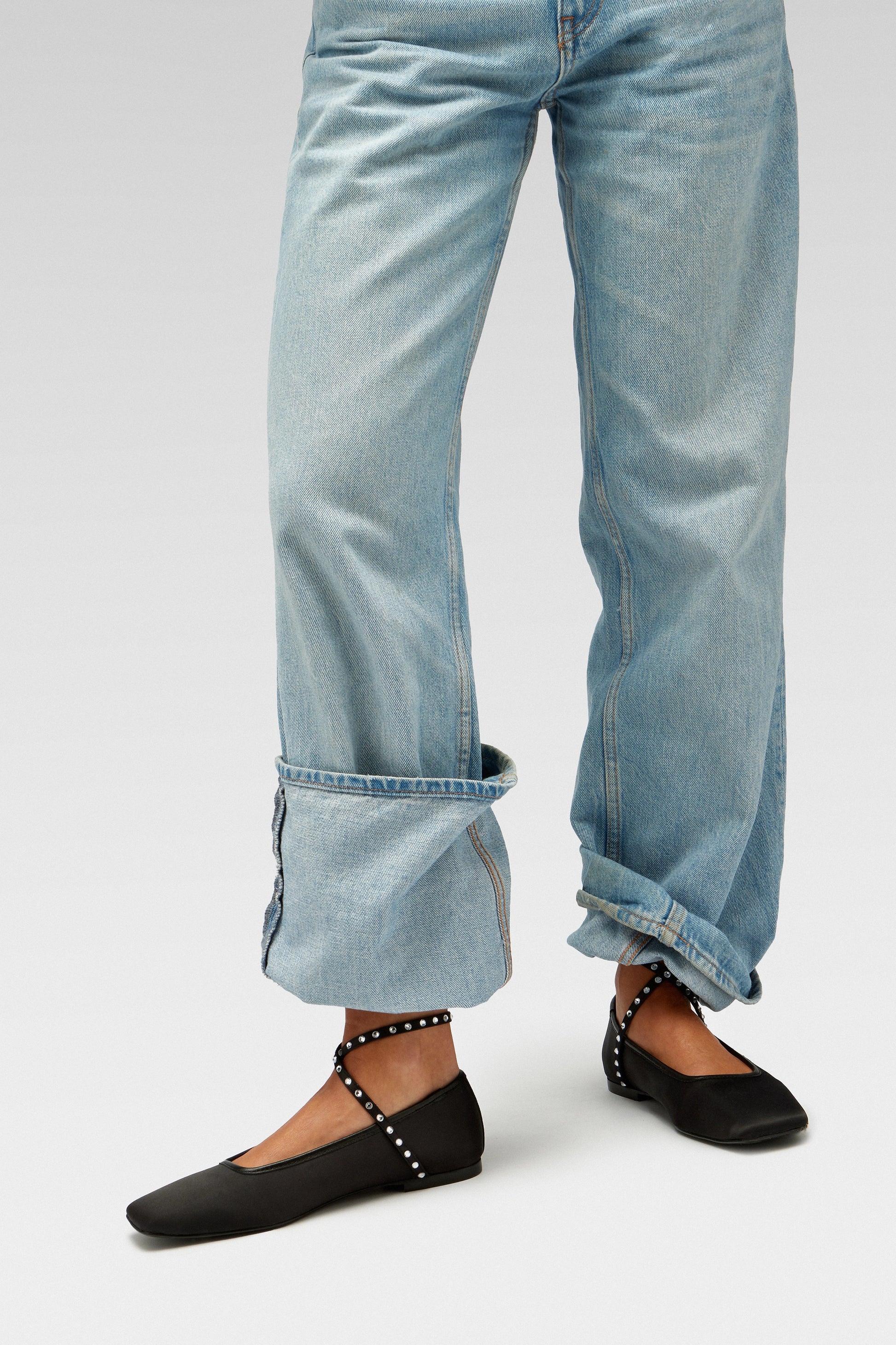 Model wearing blue jeans with EDLA Saturn black ballet flats with ankle straps embellished with crystals.