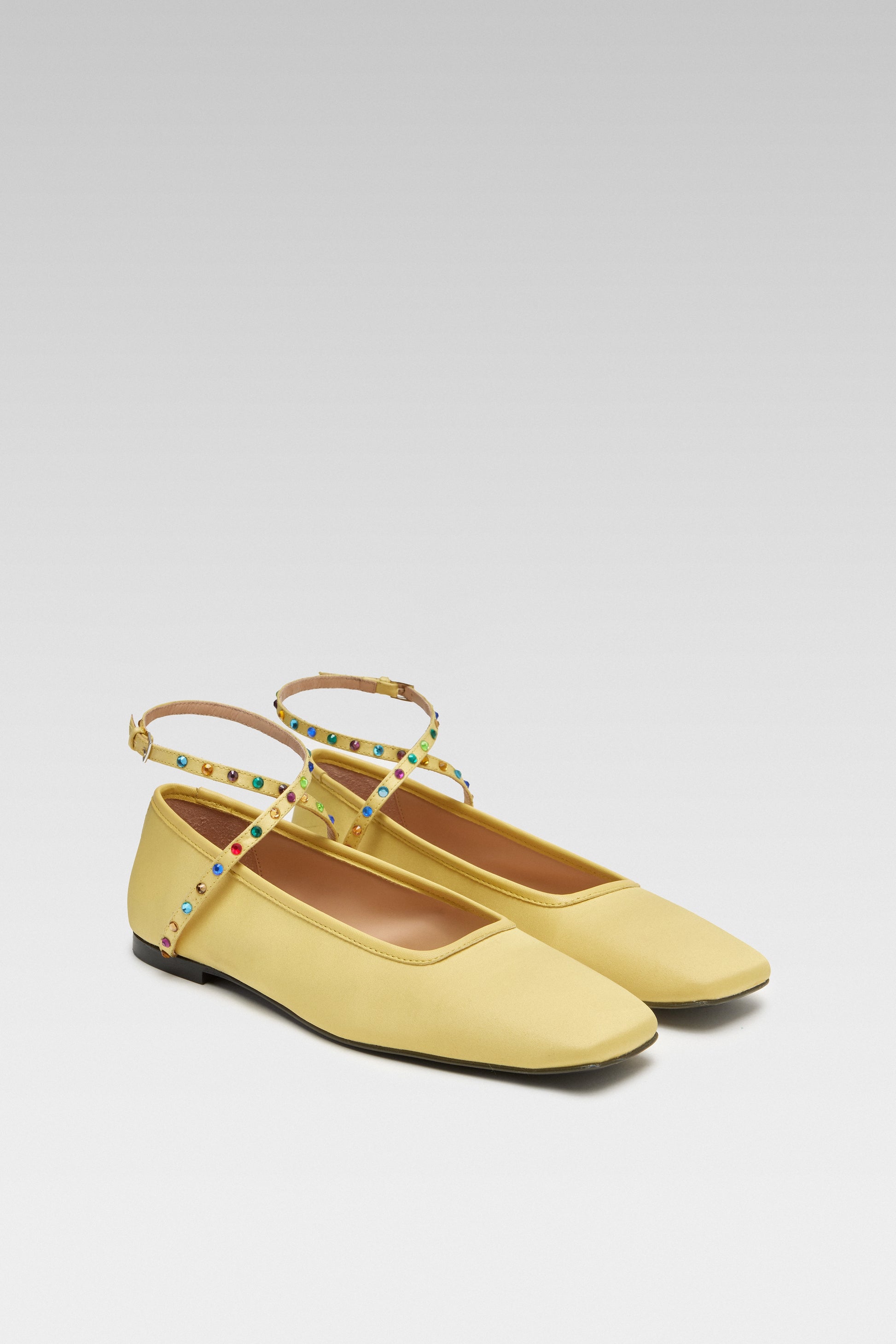 Three-quarter view of EDLA Saturn yellow ballet flats crafted from satin with a squared toe and ankle straps embellished with multicoloured crystals.